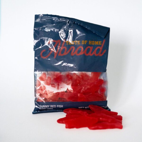 A partially opened bag of Red Swedish Fish candies with some pieces lying in front of it.